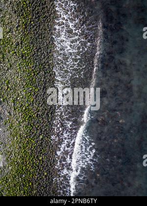 Closeup of rocky coastline with waves breaking. Portrait image, drone photo Stock Photo