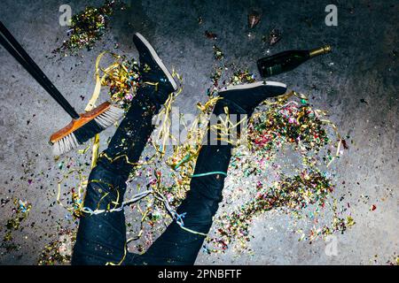 Top view of crop anonymous male lying on floor with colored paper streamers and bottle of champagne during festive occasion Stock Photo