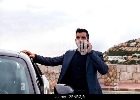 Young male worker in formal suit talking phone and looking away on street Stock Photo