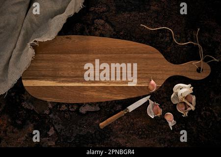 Top view of wooden oval shaped cutting board placed near knife and garlic on rough surface Stock Photo