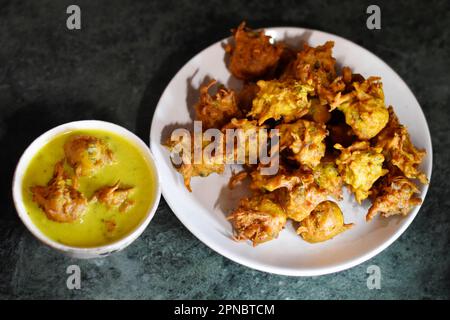 Closeup of Kadhi Pakoda or pakora and Fried onion kept in a white ceramic plate and bowl, crispy kanda bhaji, Indian cuisine, Pune, Maharashtra, India Stock Photo