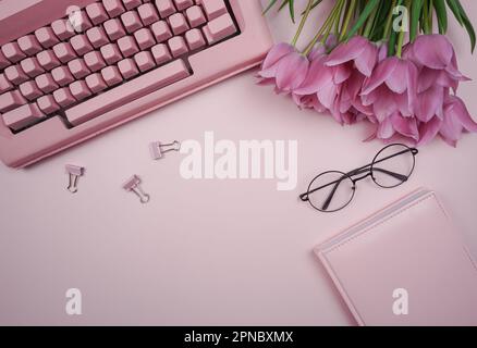 The writer's workplace is in pink. There is a typewriter on the table and there is a bouquet of tulips. Stock Photo
