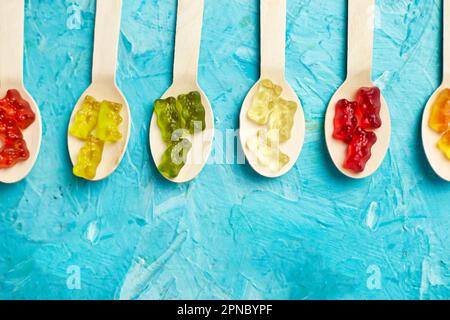 Flat lay composition with delicious jelly bears candy in wooden spoon, gummy bear on blue background, top view , copy space. Stock Photo