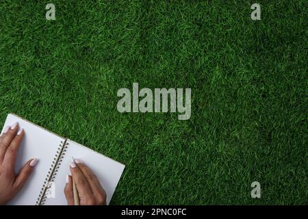 A person writing on a notebook on a field of grass.  Stock Photo