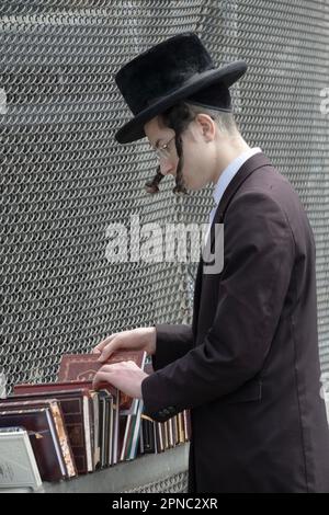 A young orthodox Jewish man with long curly peyus shops for religious books at a pop up outdoor sale in Williamsburg, Brooklyn, New York City. Stock Photo