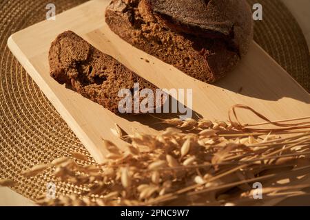 Fresh, brown, freshly baked, multi-grain and yeast-free bread on a cutting board and cereals, cut off a piece of the bread separately and copy space. Sun lights and shadows. High quality photo Stock Photo