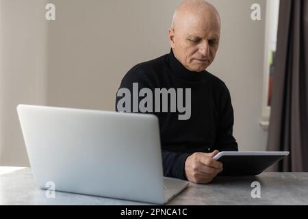 Caucasian old senior stress upset male businessman entrepreneur sitting at working desk having headache after reading graph chart report and contract Stock Photo