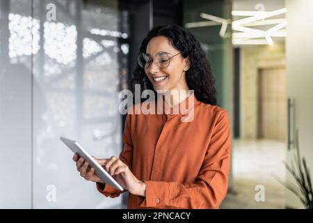 Indian female programmer standing inside the office with a tablet computer in her hands, the woman is testing a new software application. Stock Photo