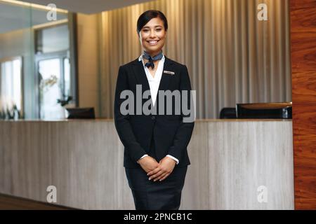 Young Asian receptionist standing confident in her formal wear, smiling and looking at the camera. Female hospitality employee working as a concierge Stock Photo