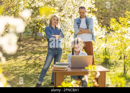 little girl with strict parents studying on laptop outdoor Stock Photo