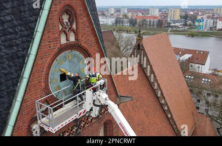 18 April 2023, Brandenburg, Frankfurt (Oder): An employee (l) from the company Bittner Glocken- und Turmuhren and a technician from the lifting platform mount the gilded hands and numerals on the southern tower clock of the Friedenskirche at a height of 38 meters (aerial view with a drone). On the same day, two employees of the Bittner company had remounted the restored and newly gilded hands and numerals of the church tower clock, which dates back to about 1900, on the clock face. The clockwork had already been restored by the company. The restoration project around the tower clock arose in 2 Stock Photo