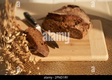 Fresh, brown, freshly baked, multi-grain and yeast-free bread on a cutting board and cereals, cut off a piece of the bread separately, the knife and copy space. Sun lights and shadows. High quality Stock Photo