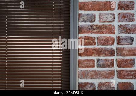 Window with brown blinds and a brick wall made of old bricks, loft interior, industrial interior as a background, close-up Stock Photo