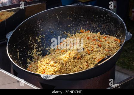Hot pilaf in large cauldron outdoors. Traditional oriental food. Street food concept. Closeup Stock Photo