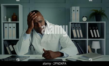 Pensive thoughtful sad african doctor ethnic elderly age man feel despair stress exhausted tired male sit at hospital think health problem depress Stock Photo