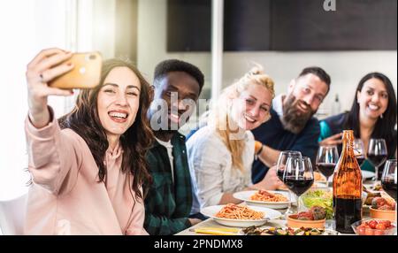 Multiethnic guys and women taking selfie for lunch in the home kitchen - Young friends having fun together in the apartment while eating delicious ita Stock Photo