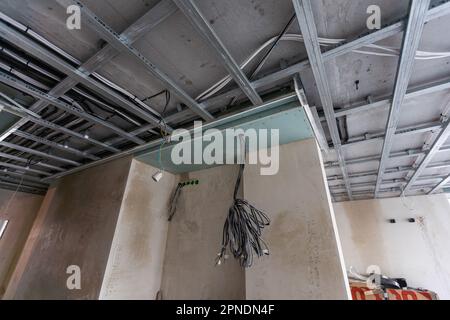 Installation of drywall. Workers are using screws and a screwdriver to attach plasterboard to the ceiling Stock Photo
