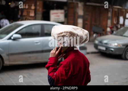 man on mobile phone on street carries arabic bread on his head, Stock Photo