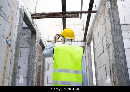 Concentrated engineer in safety vest at construction site wearing a hard helmet hat. Young professional foreman working on structure building at workplace - with copy space Stock Photo