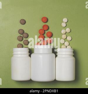 Multi-colored pills with vitamins or dietary supplements fly out of three white plastic jars on a green background Stock Photo
