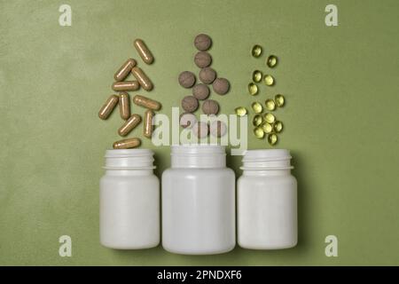 Multi-colored pills and capsuless with vitamins or dietary supplements fly out of three white plastic jars on a green background Stock Photo