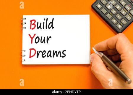 BYD build your dreams symbol. Concept words BYD build your dreams on white note on a beautiful orange background. Businessman hand. Calculator. Busine Stock Photo