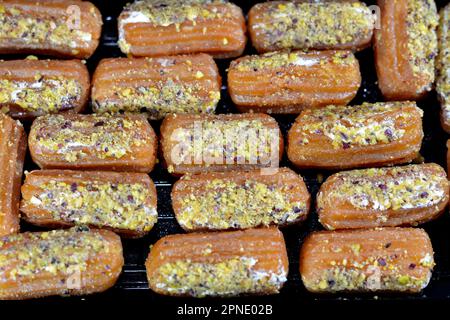 Tulumba, Bamiyeh or Balah El Sham stuffued with whipped cream and covered with pistachios and nuts, deep fried batter dessert soaked in syrup, similar Stock Photo