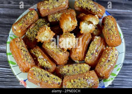 Tulumba, Bamiyeh or Balah El Sham stuffued with whipped cream and covered with pistachios and nuts, deep fried batter dessert soaked in syrup, similar Stock Photo