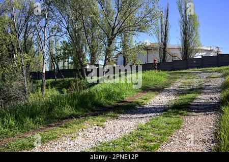 Path  on an embankment next to a boundary wall of an industrial complex in a forest Stock Photo