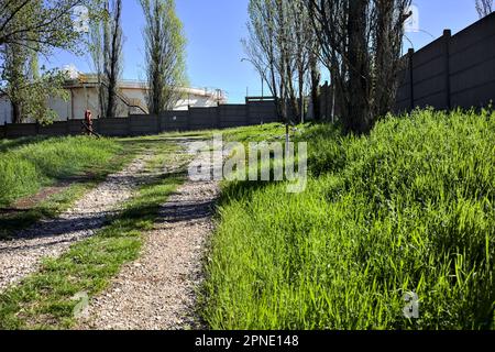 Path  on an embankment next to a boundary wall of an industrial complex in a forest Stock Photo