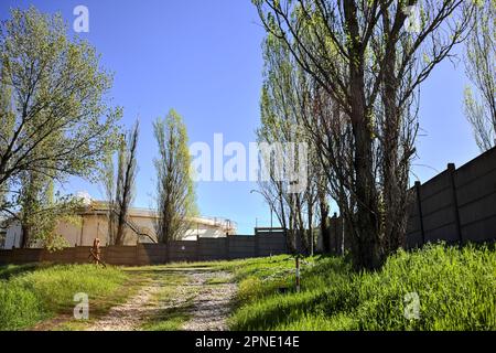 Path  on an embankment next to a boundary wall of an industrial complex in a forest Stock Photo