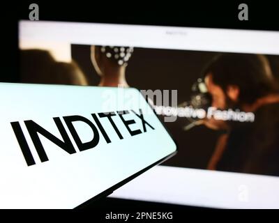 Smartphone with logo of Industria de Diseno Textil SA (Inditex) on screen in front of business website. Focus on center-left of phone display. Stock Photo