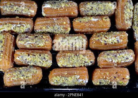 Tulumba, Bamiyeh or Balah El Sham stuffued with whipped cream and covered with pistachios and nuts, deep fried batter dessert soaked in syrup, similar Stock Photo