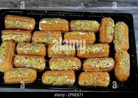 Tulumba, Bamiyeh or Balah El Sham stuffued with whipped cream and covered with pistachios and nuts, deep fried batter dessert soaked in syrup, similar Stock Photo