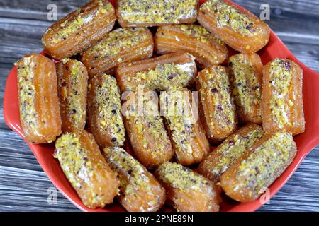 Tulumba, Bamiyeh or Balah El Sham stuffued with whipped cream and covered with pistachios and nuts, deep fried batter dessert soaked in syrup, similar Stock Photo