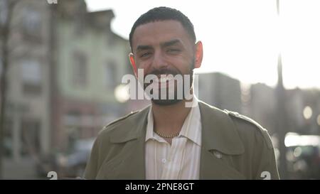 One Middle Eastern young man standing in city street smiling at camera. Tracking shot in motion of an Arab Moroccan male person with joyful expression Stock Photo