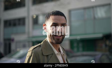 One Middle Eastern young man standing in city street smiling at camera. Tracking shot in motion of an Arab Moroccan male person with joyful expression Stock Photo