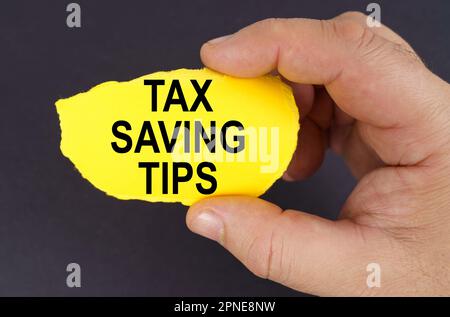 Business concept. On a black background, in the hands of a man, a yellow torn cardboard with the inscription - Tax Saving Tips Stock Photo
