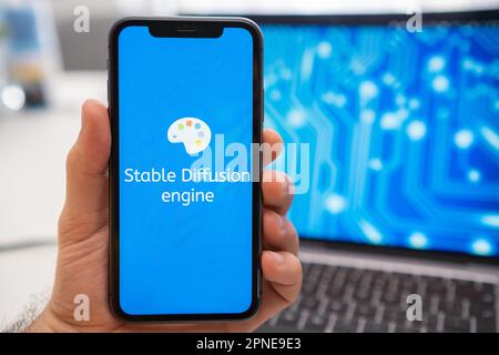 A man is holding a smartphone with a Stable Diffusion engine logo on the screen, while in the background, a laptop displays a neuronet on the splash screen. March 2023, Prague, Czech Republic  Stock Photo