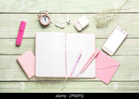 Composition with notebook, mobile phone, clock and earphones on green wooden table Stock Photo