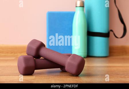 Dumbbells with fitness mat, block and bottle near pink wall