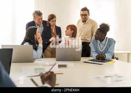 A multiethnic group of colleagues, including Caucasians, Americans, Chinese, and Africans, attentively discussing a project in front of a laptop, with Stock Photo