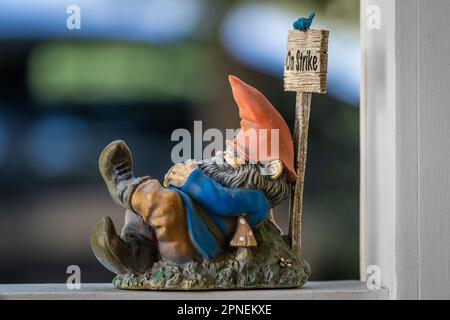 A figurine of a garden gnome sleeps against his picketting sign showing a blue bird he is on strick as Stock Photo