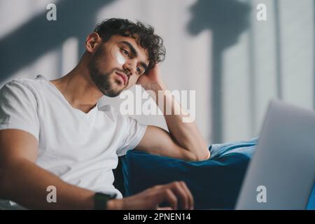 Handsome cheerful young man indoors at home on sofa using laptop computer. Education internet technology. Home comfort. Stock Photo