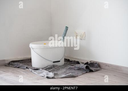 A bucket of white paint is in the corner of a room. The sockets are taped. Stock Photo