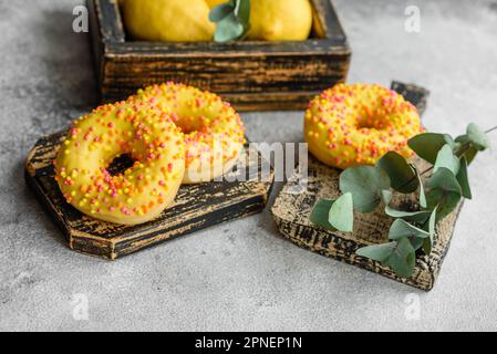 Delicious fresh donuts in yellow glaze with lemon flavor filling on textured concrete background Stock Photo