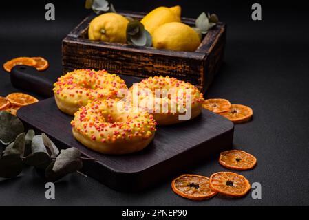 Delicious fresh donuts in yellow glaze with lemon flavor filling on textured concrete background Stock Photo