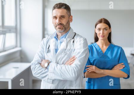 Medical services concept. Confident doctor male and female colleagues wearing coats, posing with folded arms Stock Photo