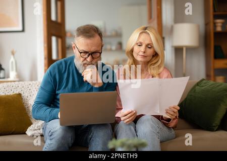 Senior Couple Using Laptop Computer Reading Bills Sitting At Home Stock Photo