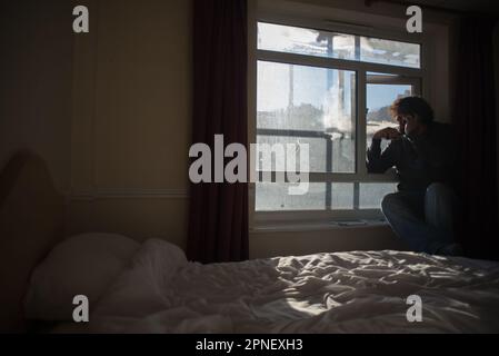 A man vapes at his hotel room window at a south British hotel Folksteone. Image taken in the Grand Burstin Hotel, Part of Britannia Hotels, Folkstone Stock Photo